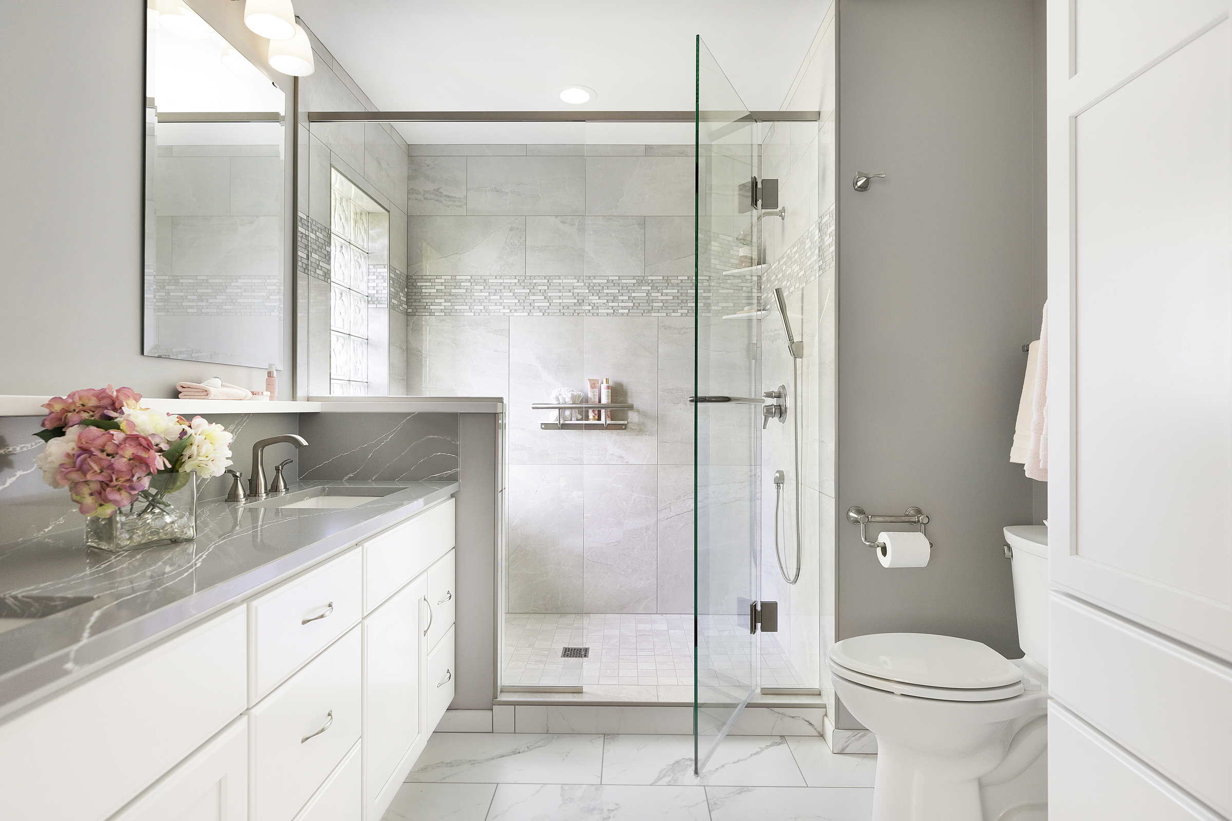 Bathroom renovation with glass walk in shower, white vanity, and large marble floor tile