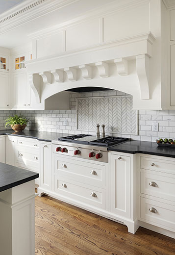 Kitchen remodel featuring large custom hood vent, black countertops,  and marble backsplash tile